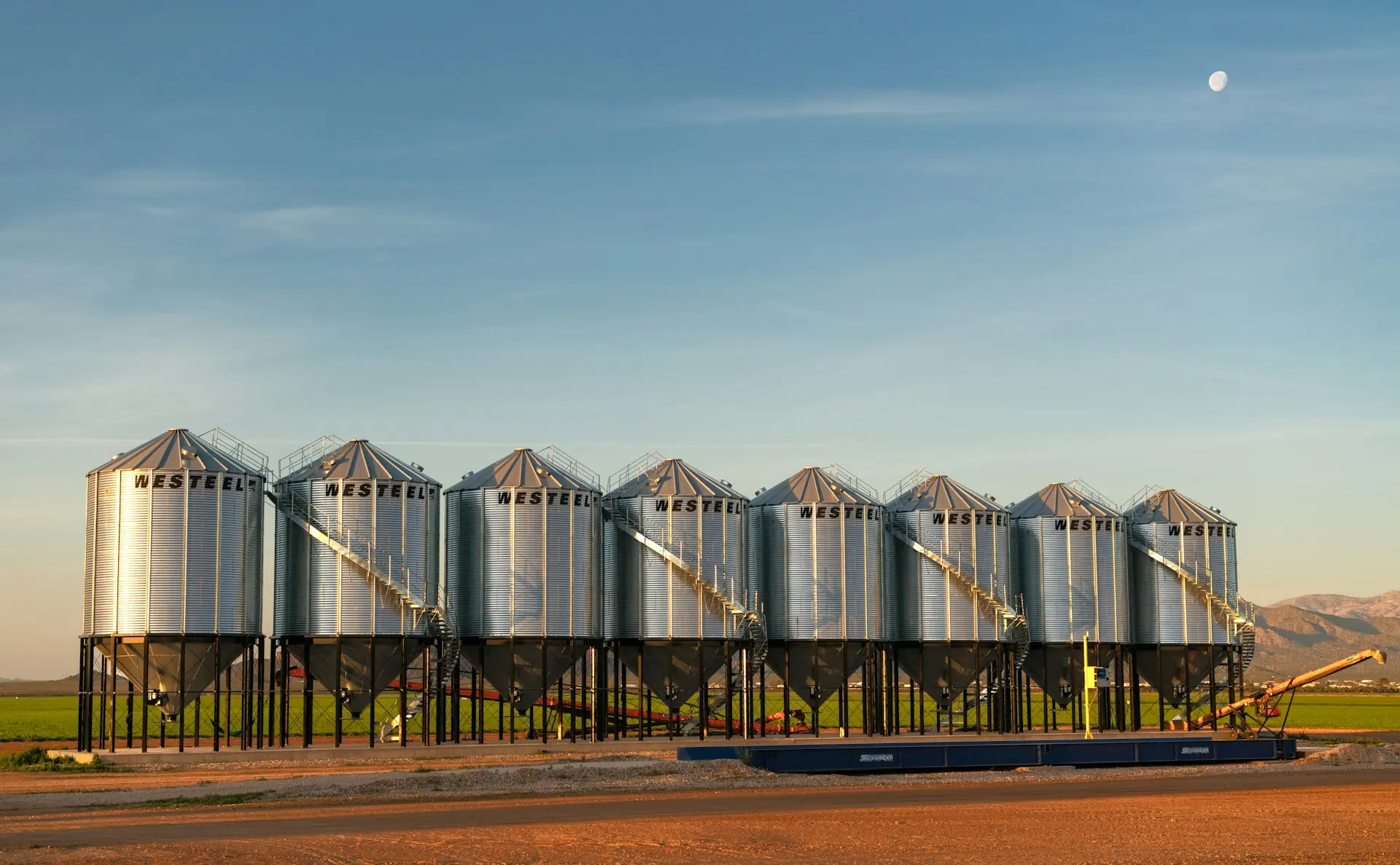 Steel grain bins at golden hour with the moon overhead